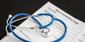 A blue stethoscope folded on top of health insurance forms.